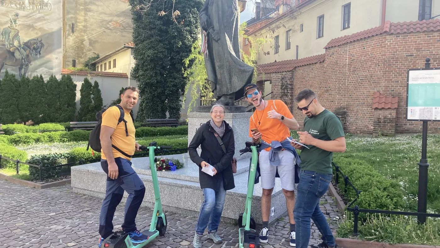 Vier junge Erwachsene mit E-Scootern vor einer Statue in Krakau, viel Spass