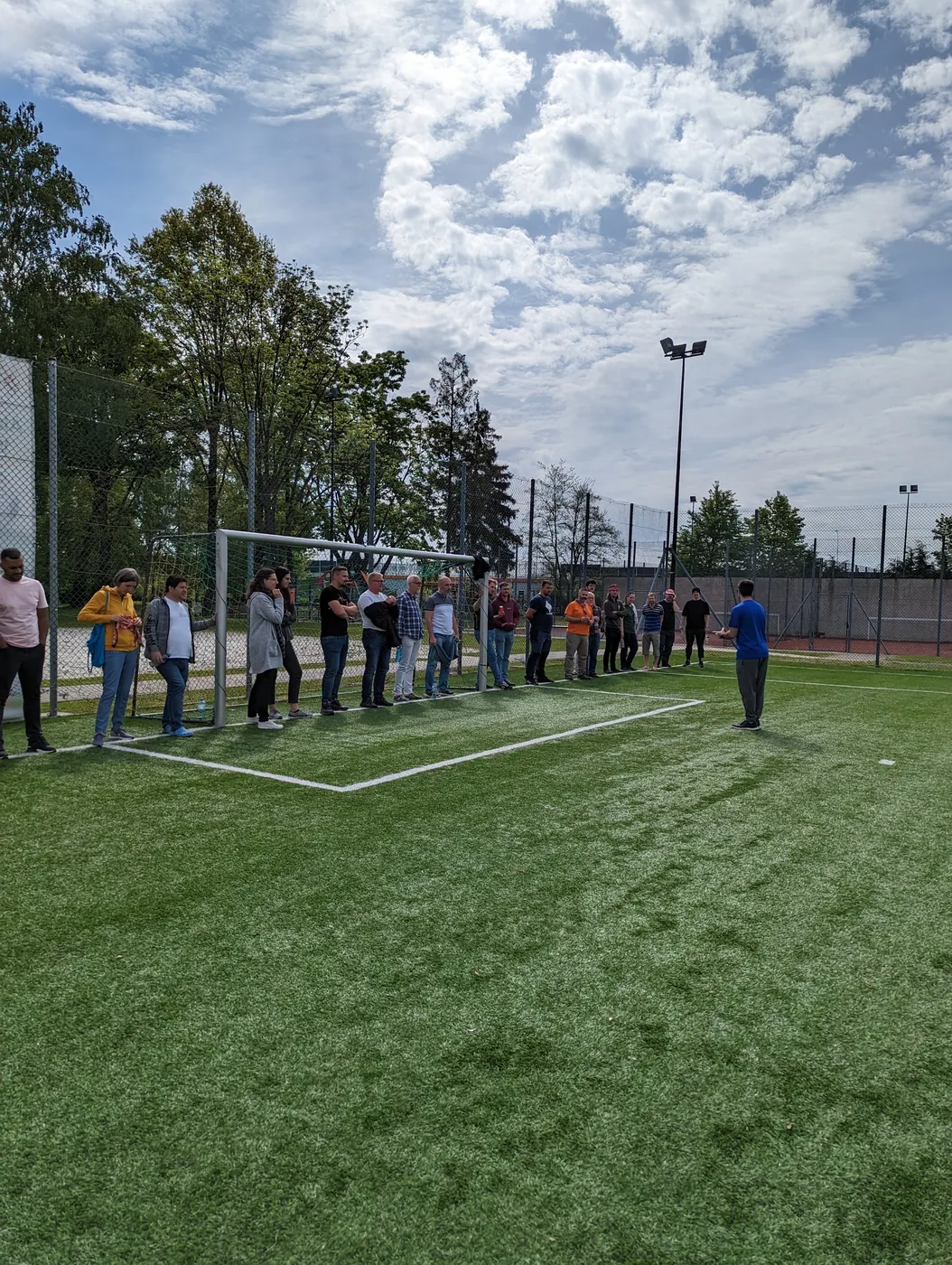Die Gruppe steht in Reihe auf dem Sportplatz und hört der Anleitung eines Leiters zu