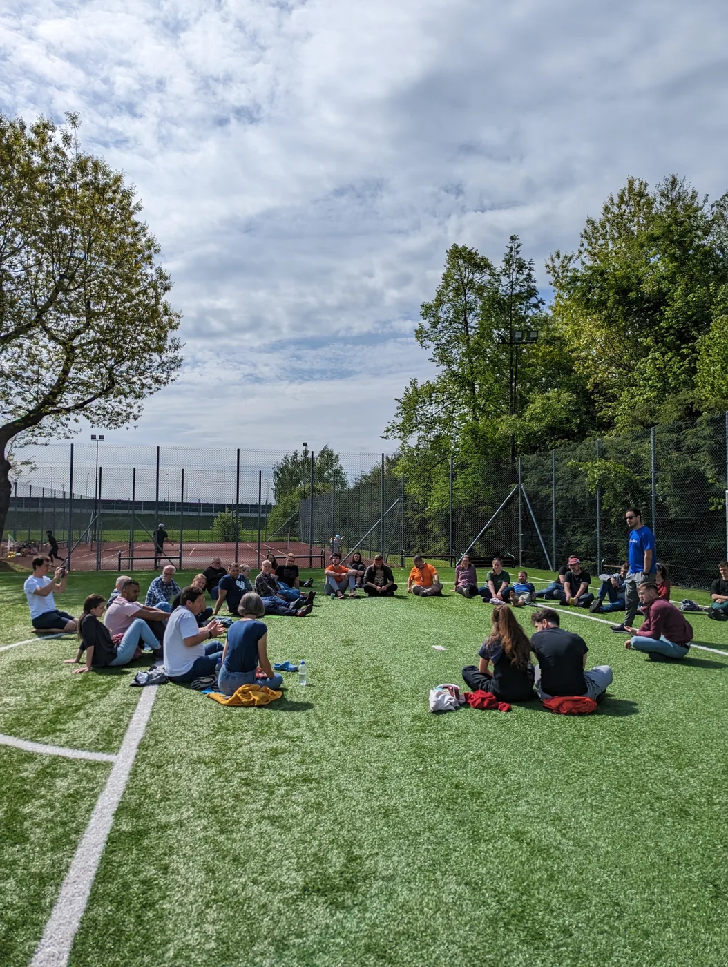 Grosser Sitzkreis der ganzen Gruppe auf dem Rasen des Sportplatzes in der Sonne