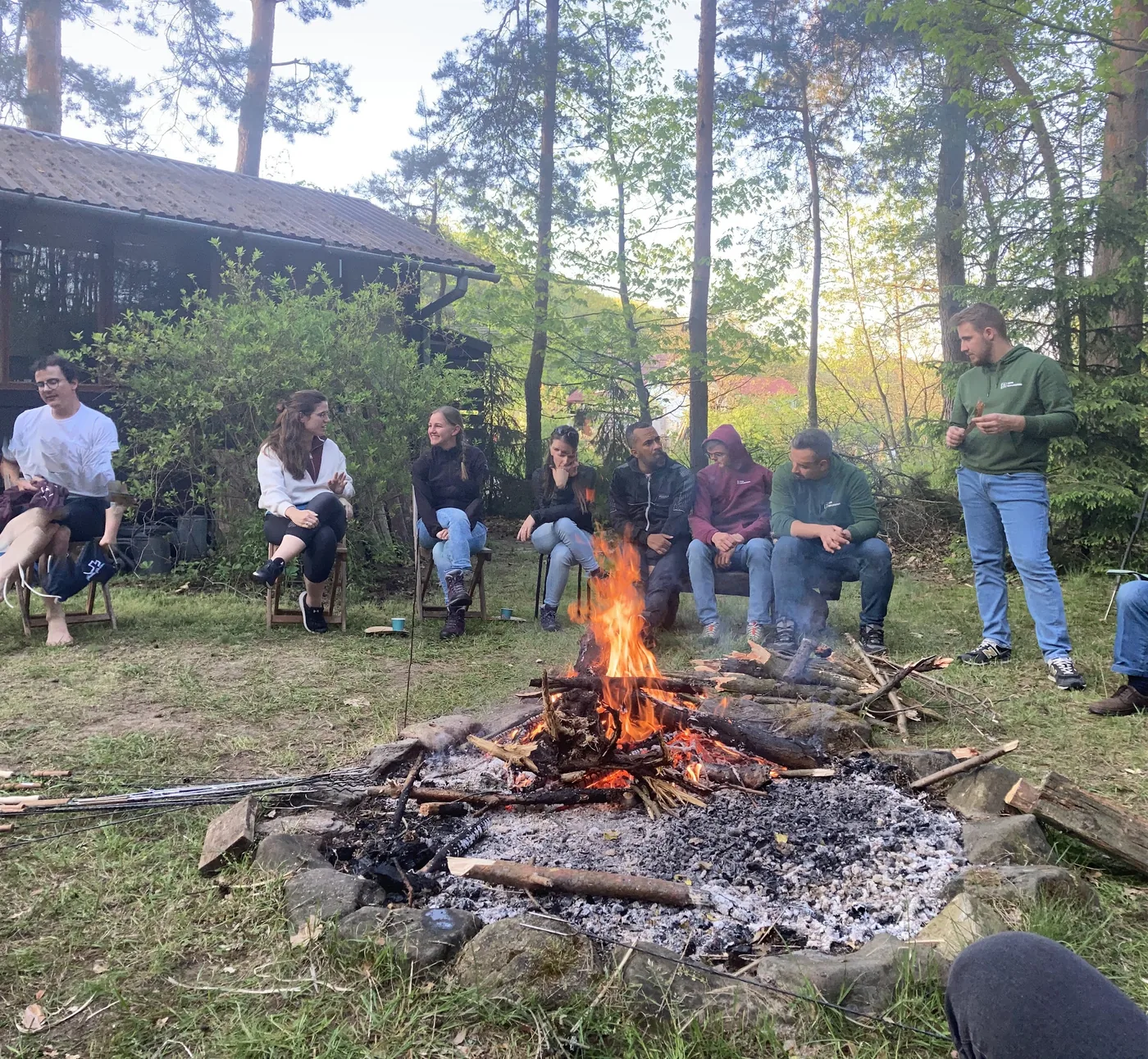 Abendliche Runde am knisternden Lagerfeuer vor der Waldhütte, eine Person erzählt