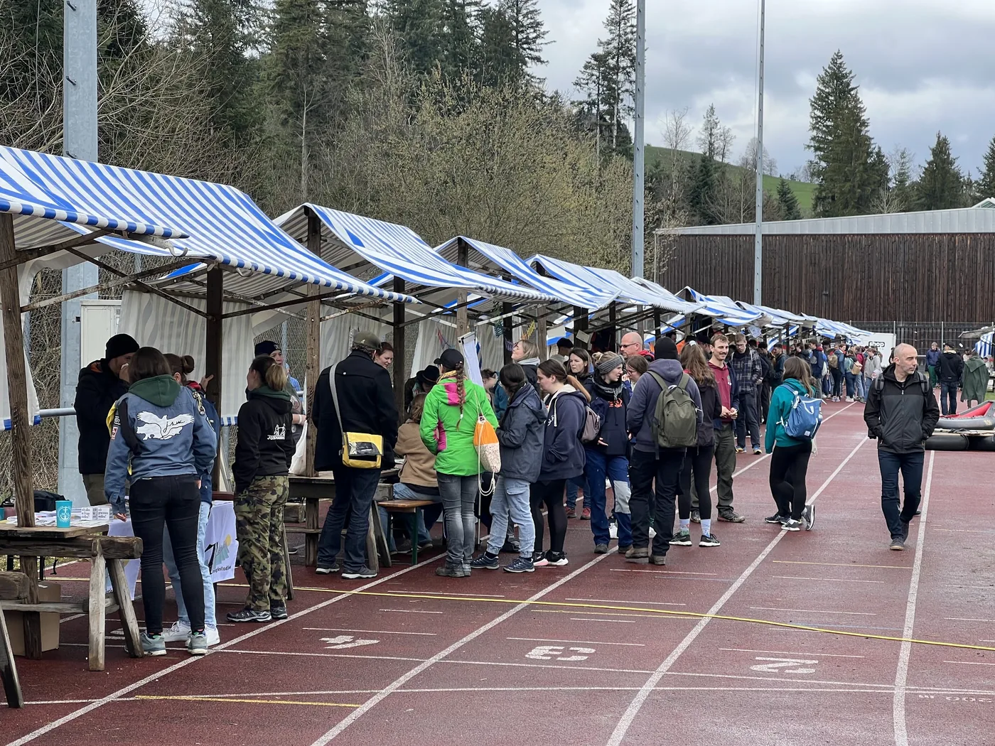 Marktstandzeile mit vielen Besuchern auf der Tartanbahn vor Waldhügeln