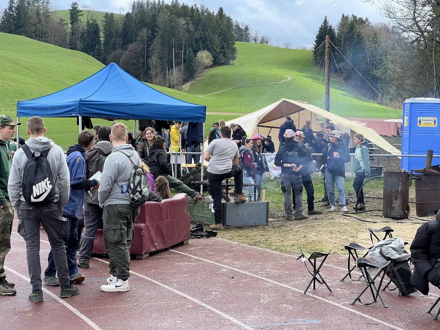 Gruppen an Zelten und Feuertonne vor grünen Hügellandschaften