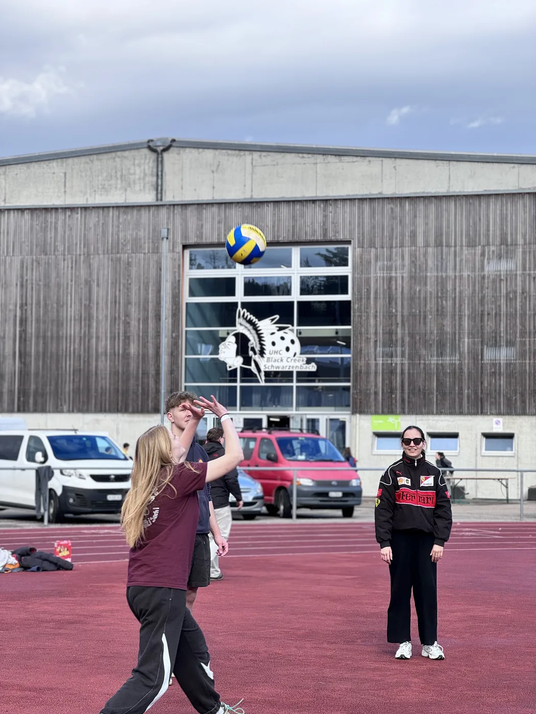 Junge Frau wirft Volleyball auf der Tartanbahn, Mitspielerin schaut zu