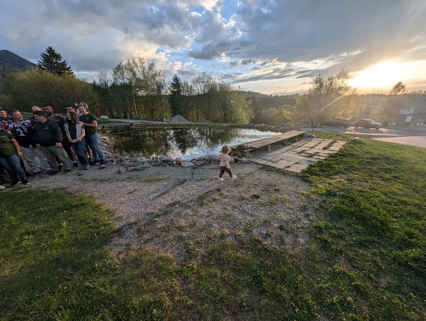 Abendstimmung am Teich: Leiter am Ufer, Kleinkind läuft zum Steg, Sonnenuntergang über den Bergen