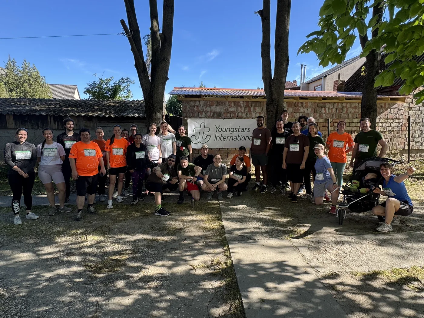 Grosses Gruppenfoto aller Teilnehmenden mit Youngstars-International-Banner vor Steinmauer