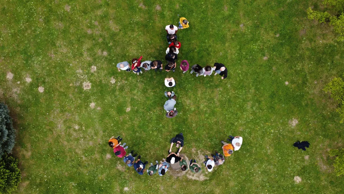 Drohnenaufnahme: Die NCM-Delegation formt als Menschenkette das Youngstars-Anker-Symbol auf einer Wiese