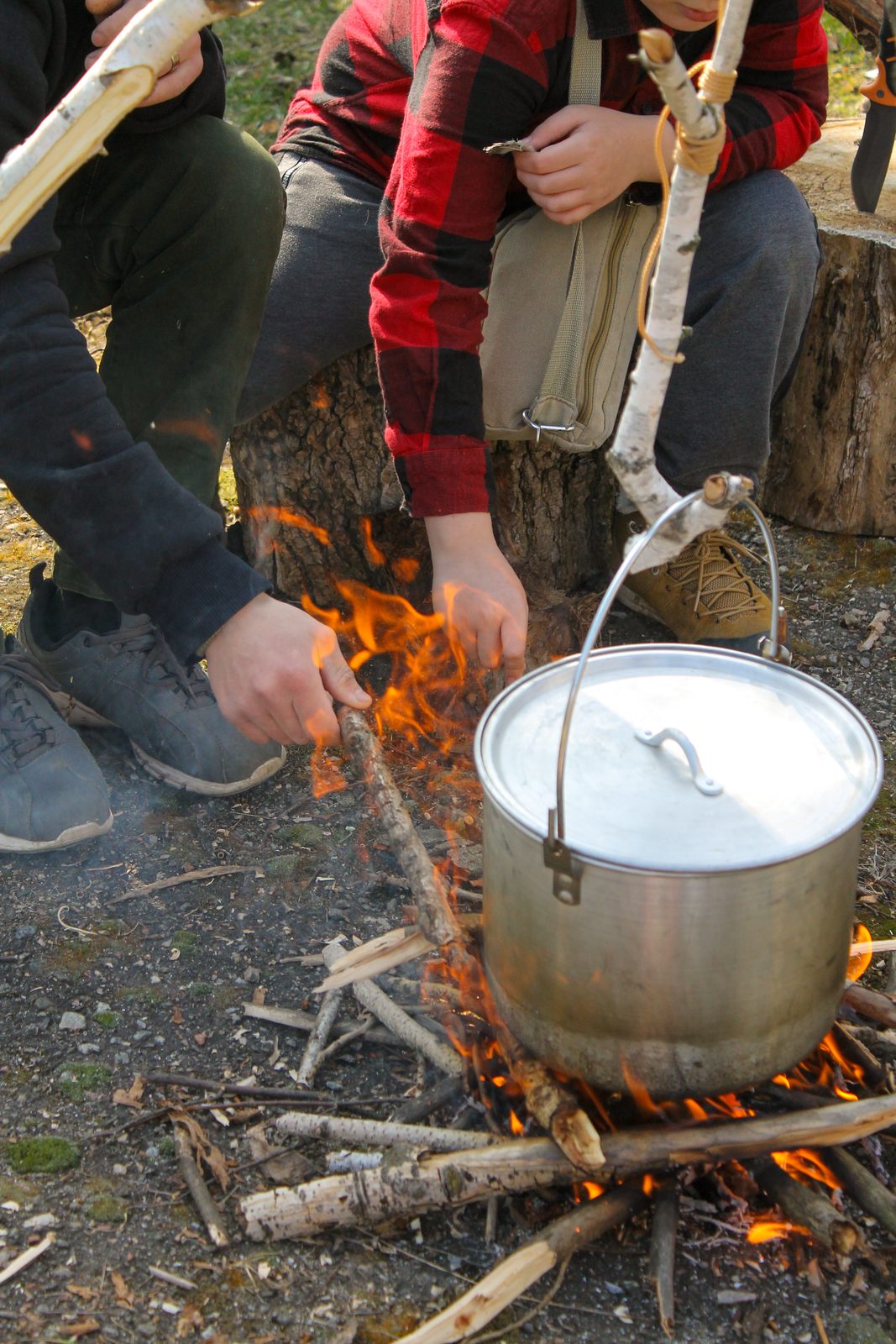Kinder kochen einen Topf über dem Lagerfeuer.